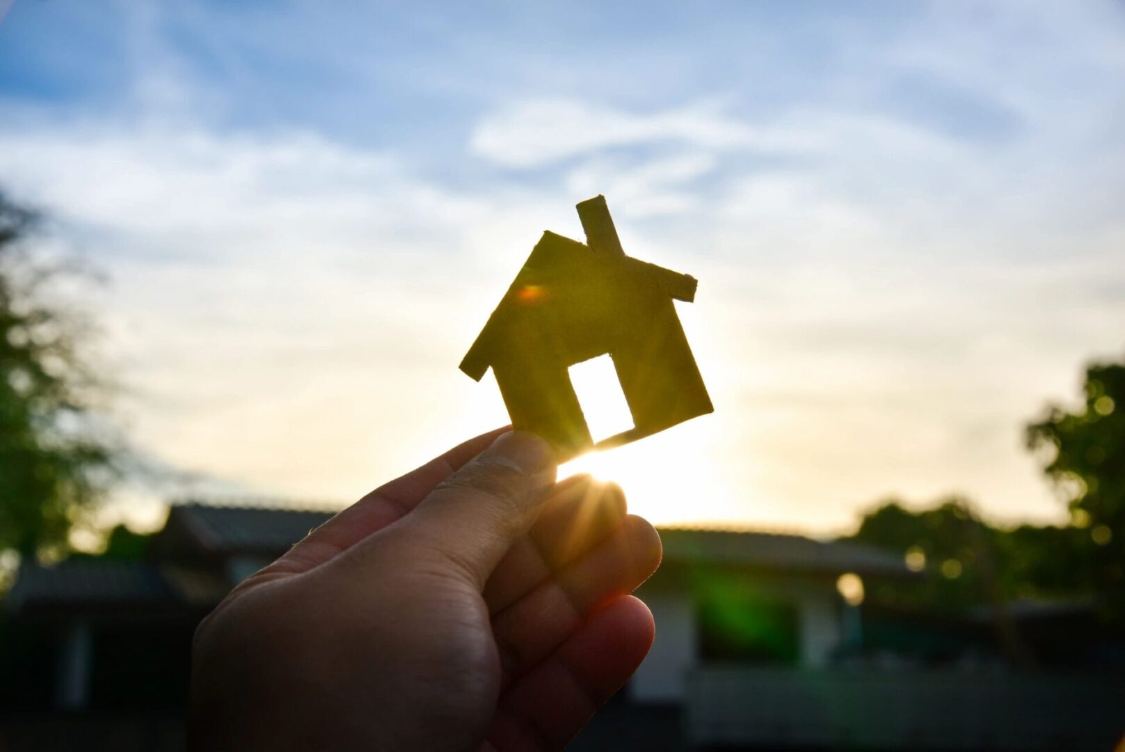 A person holding up a small house in front of the sun.